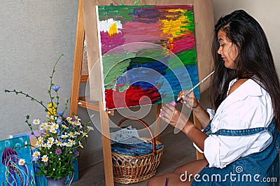 Creative pensive female painter paints a colorful abstract picture. Closeup of painting process in art workshop or home Stock Photo