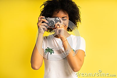 Creative woman-photographer takes photos, isolated on yellow. Stock Photo
