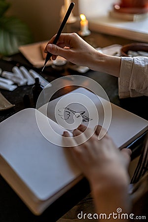 Creative work, passion, hobby. Artist sitting table with burning candles drawing ink in notebook. Stock Photo