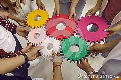 Creative young people hold colored gears of different sizes symbolizing coordinated teamwork. Stock Photo