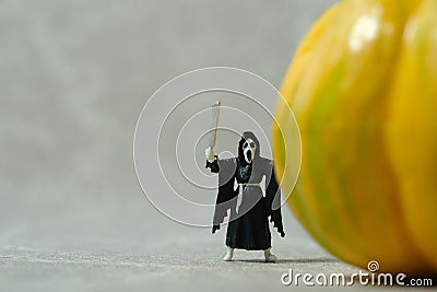 Creepy ghost with face mask standing behind pumpkin. Miniature people photography Stock Photo