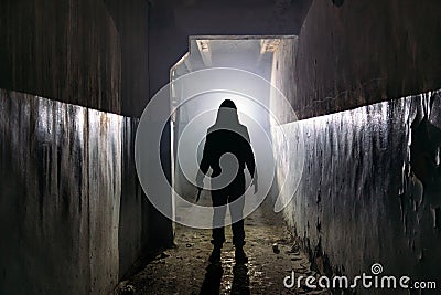 Creepy silhouette of unknown man with knife in dark abandoned building. Horror about maniac concept Stock Photo