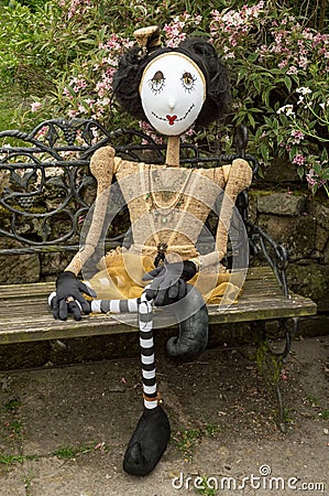 Creepy steampunk doll sitting on garden bench. Leg crossed. Stock Photo