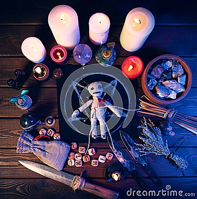 Creepy voodoo doll on dark scary spiritual wizardry table with candles and magic attributes for halloween sorcery and Stock Photo