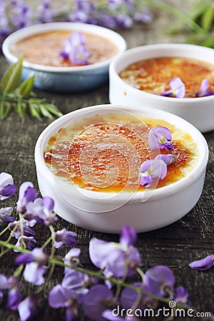 Creme brulee, french traditional dessert, three portions, flowering purple wisteria dressing Stock Photo