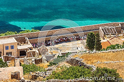 CRETE, GREECE - JULY 08 2023: Groups of tourist shelter from the sun in the shade from a large wall on the ancient fortress island Editorial Stock Photo