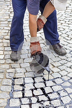 Crew member pouring molten pitch from a tar bucket Stock Photo