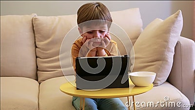 Crian?a que usa o PC da tabuleta na cama em casa O menino bonito no sof? est? olhando desenhos animados, est? jogando jogos e est filme Crian?a que usa o PC da tabuleta na cama em casa O menino bonito no sof? est? olhando desenhos animados, est? jogando jogos e est filme