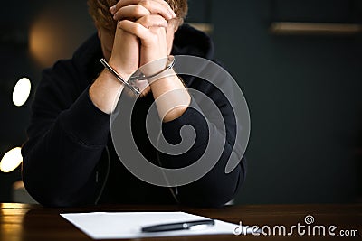 Criminal in handcuffs with confession at desk indoors Stock Photo