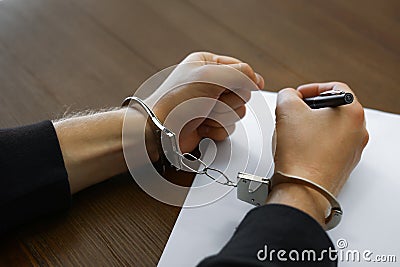 Criminal in handcuffs writing confession at desk, Stock Photo