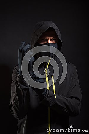 The criminal in the mask puts on a glove. Preparation for robbery Stock Photo