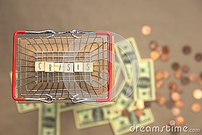 Crisis written with wooden cubes in iron shopping basket with Money coins and bills on the background, Business and Financial Stock Photo