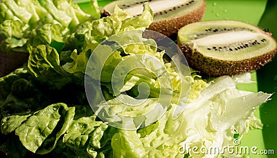 Crisp fresh lettuce with two half juicy ripe kiwi fruit on plastic plate. Green background. Salad leaf. Organic healthy food. Stock Photo