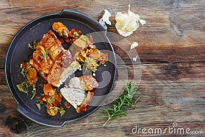 Crispy roast pork with vegetables, rosemary and garlic on a rust Stock Photo