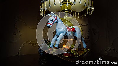 Cristmas presents. A toy, a white rocking horse, small gifts, a green ball, a pine cone. Night light. Zone light on gold fabric. Stock Photo