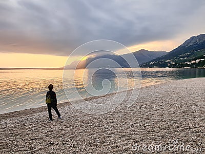 A boy stands on a pebble beach in the evening and admires the scenery Stock Photo