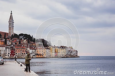 CROATIA, ROVINJ - March 29, 2018, Man fishing by the sea near colorful old town Rovinj, Istria, Croatia Editorial Stock Photo
