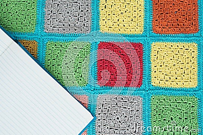 crocheted lace tablecloth of multicolored squares ornament, sheet of notebook, top view, place for text, natural wool Stock Photo