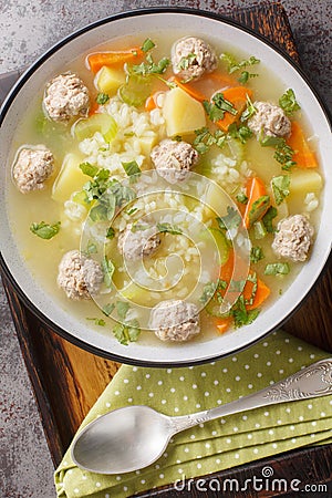 Crockpot Rice soup with meatballs, vegetables and herbs close-up in a bowl. Vertical top view Stock Photo
