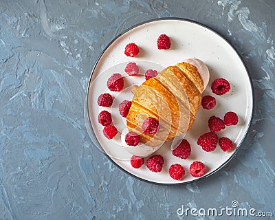 Croissant with raspberry filling and icing and fresh raspberries on a light round plate Stock Photo