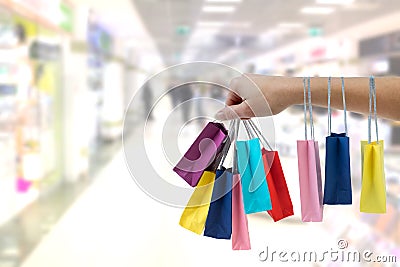 Crop female hand holding colorful paper bags on background of shopping center. Stock Photo