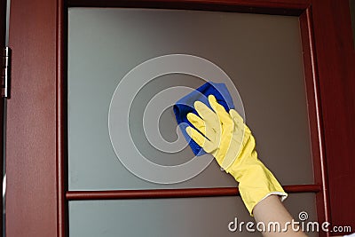 Crop of housewife hands wearing yellow gloves, cleaning dirty window. Stock Photo