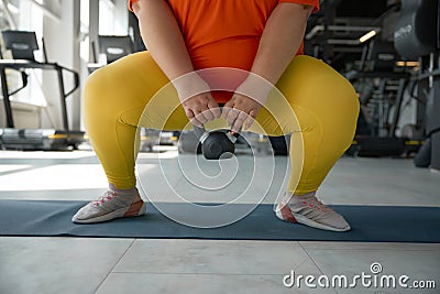 Crop of overweight obese woman squatting with kettlebell while training at gym Stock Photo