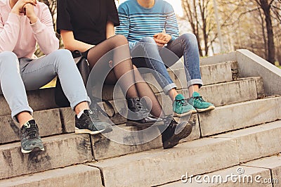 Crop photo of group of friends Millennials students teenagers sitting at city street, friendship, close up focus on feet Stock Photo