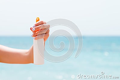 Croped image of woman`s hand holding sunblock spray at the beach Stock Photo