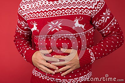 Cropped closeup photo of man in red and white christmas sweater holding his hurting stomach on isolated red background Stock Photo