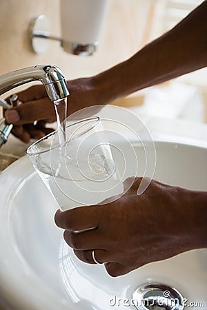 Cropped hands of man filling drinking glass at sink Stock Photo