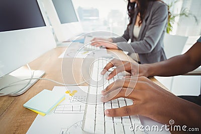 Cropped hands typing on keyboard at computer desk with coworker Stock Photo