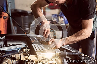 Cropped hands of unrecognizable mechanic. Close up. Repairman with screwdriver and shining lamp working under car hood Stock Photo