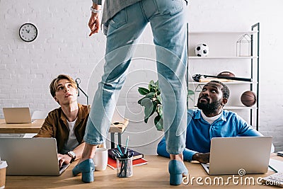 cropped image of female standing on table and pointing by finger to two multicultural businessmen working Stock Photo