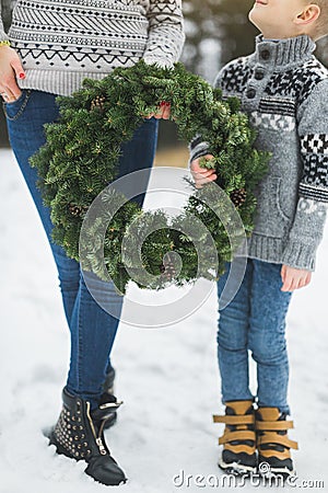 Cropped image of legs of mother and son, holding together beautiful Christmas wreath, standing outdoors in winter park Stock Photo
