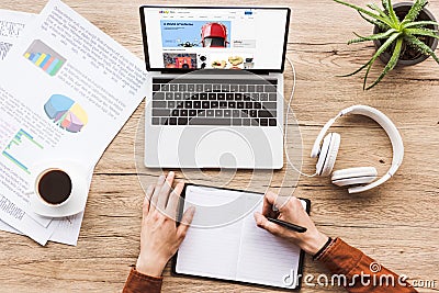 cropped image of man working at table with laptop with ebay logo, headphones, textbook, pen, infographics, coffee cup Editorial Stock Photo