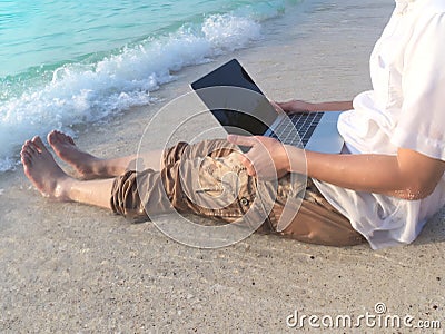 Cropped image of relaxed young Asian man with laptop sitting on sand of tropical beach in vacations day. Stock Photo