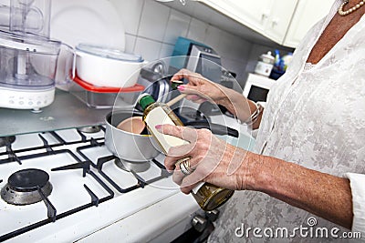 Cropped image of senior woman adding olive oil to saucepan at kitchen counter Stock Photo