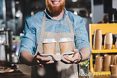 cropped image of smiling male barista holding two disposable cups of Stock Photo