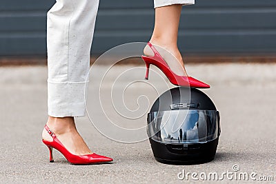 cropped image of woman in red high heels putting leg on motorcycle helmet on street Stock Photo