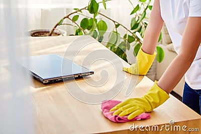 Cropped image of woman in white shirt and yellow protective rubber gloves cleaning at home and wiping dust on wooden tablel. Stock Photo