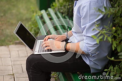 Cropped image of young man sitting at on the bench in the park, using a laptop. Stock Photo