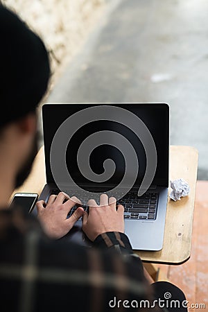 Cropped image of a young man working on his laptop sitting at wooden table Stock Photo