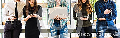 Cropped photo of Group of friends standing on table and everyone use his divices in modern office room. Together fun in device. Stock Photo