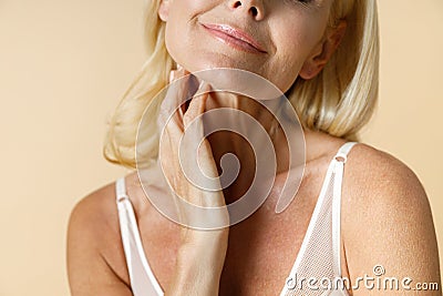 Cropped portrait of beautiful mature blonde woman in white underwear smiling, touching her neck while posing isolated Stock Photo