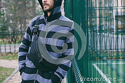 Cropped portrait of young bearded man in striped hoodie with black leather crossbody bag. Street wear, fashion city accessories Stock Photo