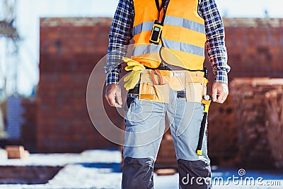 Cropped shot of builder in reflective vest and toolbelt standing Stock Photo