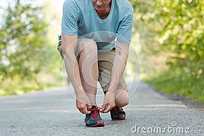 Cropped shot of elderly male athlete ties shoelaces, takes rest after jogging exercise, wears sportswear, poses outdoor. Man runne Stock Photo