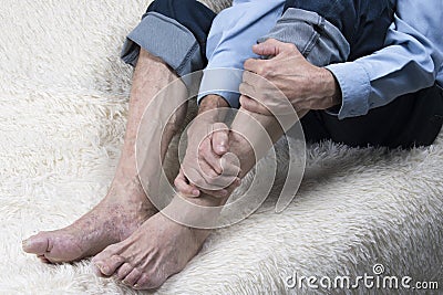 Cropped shot of elderly man sitting on sofa and suffering from foot pain. Huckle-bone disease, arthritis Stock Photo