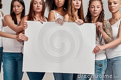 Cropped shot of group of confident diverse women in white shirt and casual denim jeans holding, standing with blank ad Stock Photo